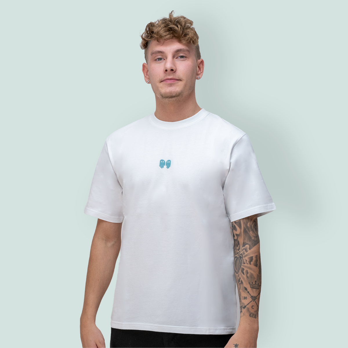 En ung mann iført en t-skjorte med et logo i midten av brystet, poserer foran en lysgrønn bakgrunn.